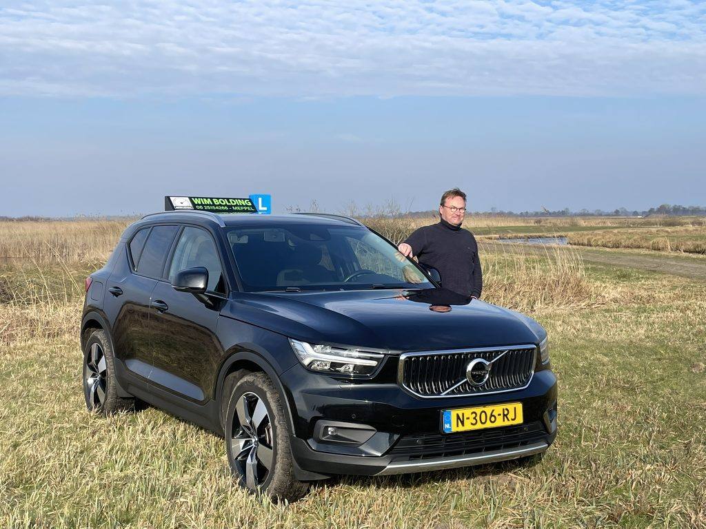 Wim Bolding naast zijn zwarte Volvo lesauto met daklichtbak in het buitengebied bij Meppel